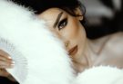 Close-up of a bride's face partially hidden by a feather fan, exuding elegance and mystery. — Blue Topaz Diamond Engagement R