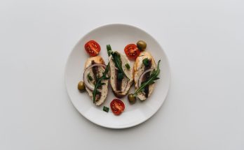 A top view of delicious bruschetta with anchovies, olives, and cherry tomatoes on a white plate. — Puppy Food - Setting It Up